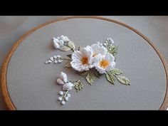 a white flower is sitting on top of a gray fabric and wood hoop with beading