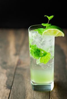 a glass filled with ice and lime on top of a wooden table