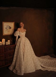 a woman in a white dress standing next to a dresser with candles on the table