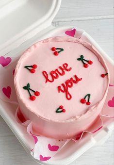 a pink cake with the words i love you written on it sitting in a plastic container