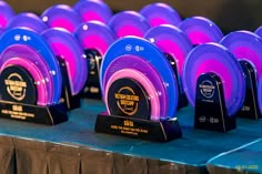 several awards are displayed on a table with purple and blue plates in the middle, along with black stands