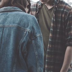 two people standing next to each other in front of a building and one person is wearing a jean jacket