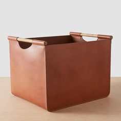 a brown leather storage bin with handles on a wooden table, ready to be used as a planter