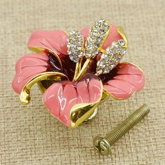 a pink flower brooch sitting on top of a piece of cloth next to a screw