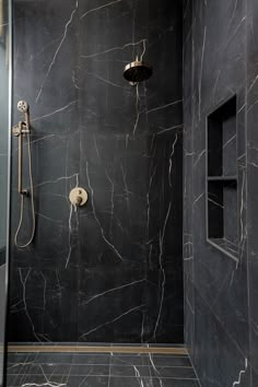 a walk in shower sitting next to a black tiled wall and floor covered in marble