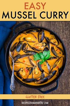 a pan filled with yellow curry and mussels on top of a wooden table