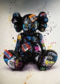 a black teddy bear covered in graffiti sitting on top of a white surface with splattered paint all over it