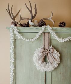 a green cabinet with two antlers and a wreath hanging on it