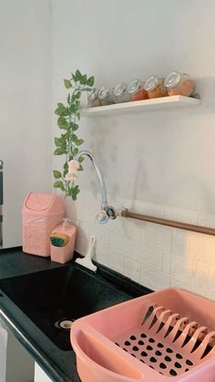 a kitchen sink with pink utensils on the black countertop and shelves above it