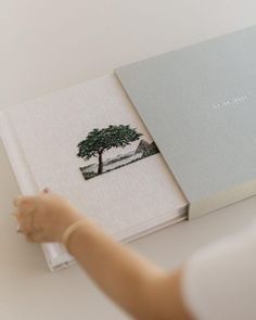 a person is holding an open book with a tree on the front and bottom cover