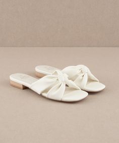 DESCRIPTION: A minimalist's dream, this knotted slide is perfectly made for any outfit. MATERIAS: Upper Material: Vegan Leather Upper Cream/Almond: Suede Upper Insole Material: Padded Insole Sole or Heel Material: White: Printed Heel Cream/Almond: Suede Wrap Heel DETAILS: Brand: Oasis Society Size Run: B18 Heel Height: 0.75" Types of Closures: Slip On Hoco Shoes Flats, White Sandals Flat, White Flat Sandals, Sandal Slippers, Random Products, Greece Trip, Womens Sandals Summer, Wedding 2024, Wrap Heels