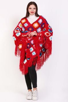 a woman wearing a red shawl with flowers and fringes on the sides, standing in front of a white background