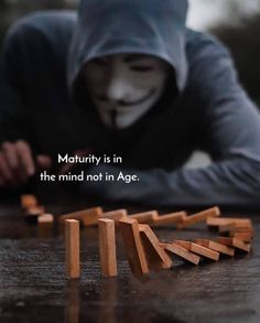 a person wearing a hoodie is playing with wooden dominos on a table that says, maturity is in the mind not in age