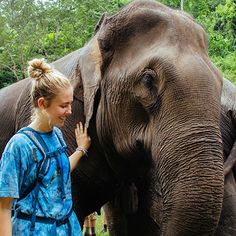 a woman standing next to an elephant with her hand on it's trunk