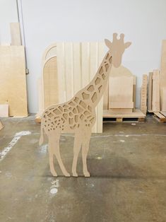 a wooden giraffe standing in front of some unfinished wood pieces on the floor