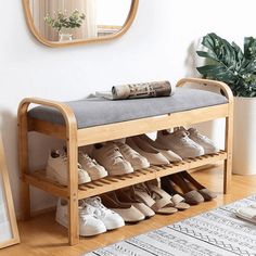 a wooden shoe rack filled with shoes next to a mirror and potted plant on the floor