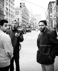 three men are standing on the street corner talking to each other and one man is wearing a beanie