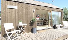 a wooden deck with two chairs and a table on it, next to a building