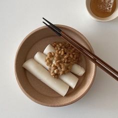 two chopsticks and some food in a bowl on a white table with a cup