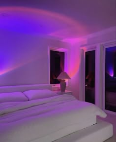 a large bed sitting under a purple light in a bedroom