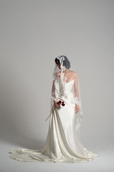 a woman in a white wedding dress holding a red flower and wearing a long veil