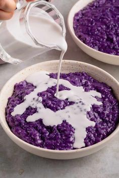 a person pouring milk into a bowl filled with purple rice and another bowl is in the background