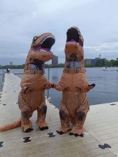 two inflatable dinosaurs are standing on a dock near the water with their mouths open