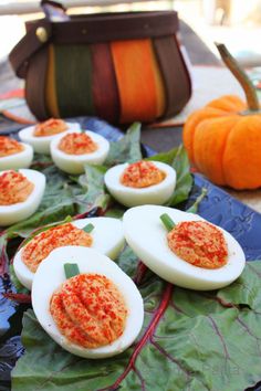 deviled eggs with red sauce on them are sitting on leafy leaves next to a pumpkin