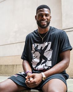 a man sitting on the ground with his hands in his pockets and smiling at the camera