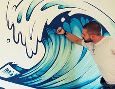 a man painting a mural on the side of a building with blue and white waves