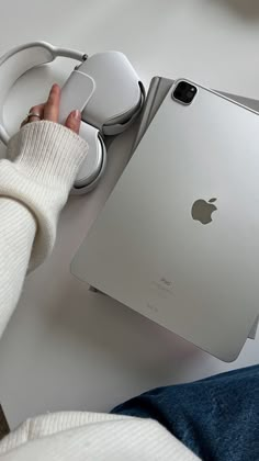 a person holding an apple mouse next to a laptop computer on a white desk with headphones