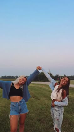 two girls are standing in the grass with their arms outstretched