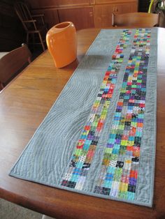 the table runner is made from blocks of quilted fabric and has a vase on it