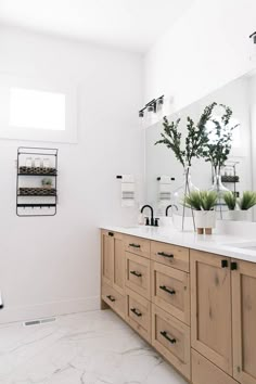 a white bathroom with wooden cabinets and marble counter tops, two planters on the wall