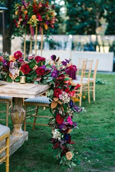 a table with flowers and candles on it in the middle of some grass, surrounded by chairs