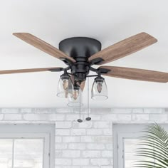 a ceiling fan with three light bulbs and two glass shades on the blades in front of a brick wall