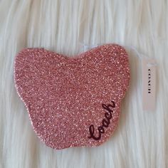 a pink heart with the word love written on it sitting on a white fur surface