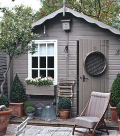 a small garden shed with potted plants in the front and an outdoor chair on the side