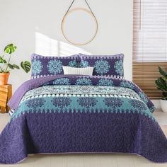 a bed with purple and blue bedspread in a room next to a potted plant