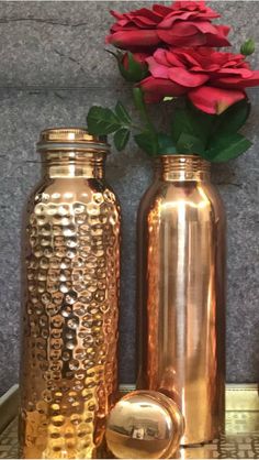 two gold vases with red flowers in them on a tray next to a wall