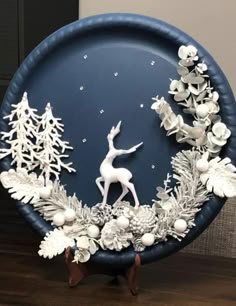 a blue plate with white decorations on it and a deer standing in the snow surrounded by pine cones