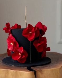 a black hat with red flowers on top sitting on a wooden table in front of a white wall