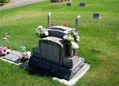 a grave with flowers on it in the middle of a grassy area next to a road