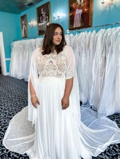 a woman standing in front of a rack of wedding dresses