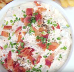 a white bowl filled with bacon and ranch dip next to chips on a table top