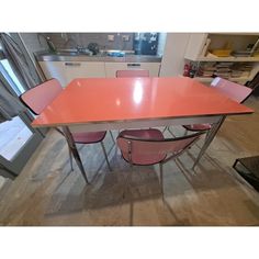 an orange table with four pink chairs around it in a room filled with other furniture