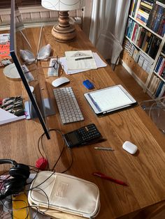 a wooden desk topped with lots of books and computer equipment next to a lamp on top of a hard wood floor