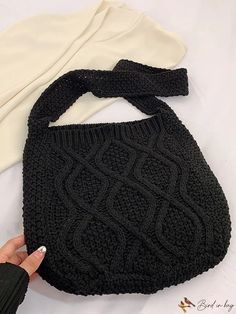 a hand holding a black knitted purse