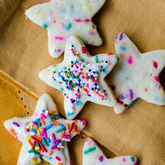 four decorated sugar cookies with sprinkles on a brown cloth next to each other