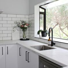 a kitchen with white cabinets and counter tops next to a window that looks out onto the trees outside